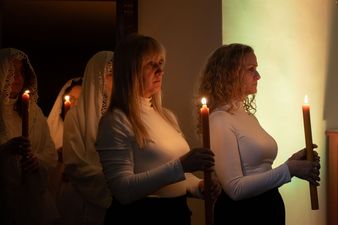 kobiety w bieli idą z zapalonymi świecami