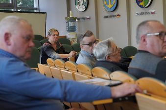 Profil siedzących uczestników spotkania. W tle na ścianie wiszą herby miast partnerskich, m.in. Karwiny
