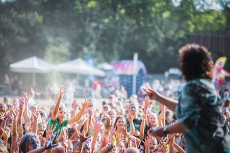 Widok zza pleców prowadzącego na tłum dzieci z uniesionymi rękami podczas festiwalu kolorów