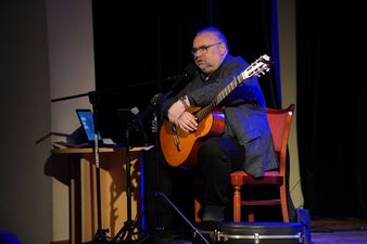 Siedzący z gitarą akustyczną artysta przemawiający do widowni