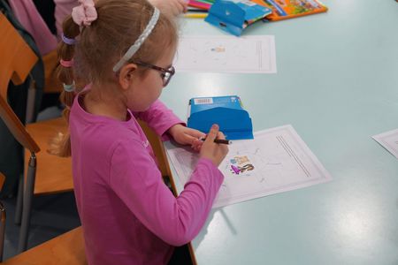 Ujęcie z boku dziewczynka w okularach siedzi i trzyma w ręku mazak