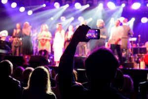 Widok na scenę podczas koncertu - na pierwszym planie osoba robiąca zdjęcia.