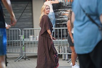 Blondynka w długiej, brązowej narzutce przechodząca w strefie plenerowej wydarzenia