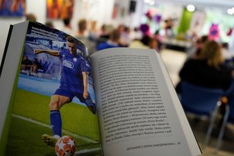 otwarta książka Ogniste Serca i zdjęcie piłkarza w niebieskim stroju kopiącego piłkę