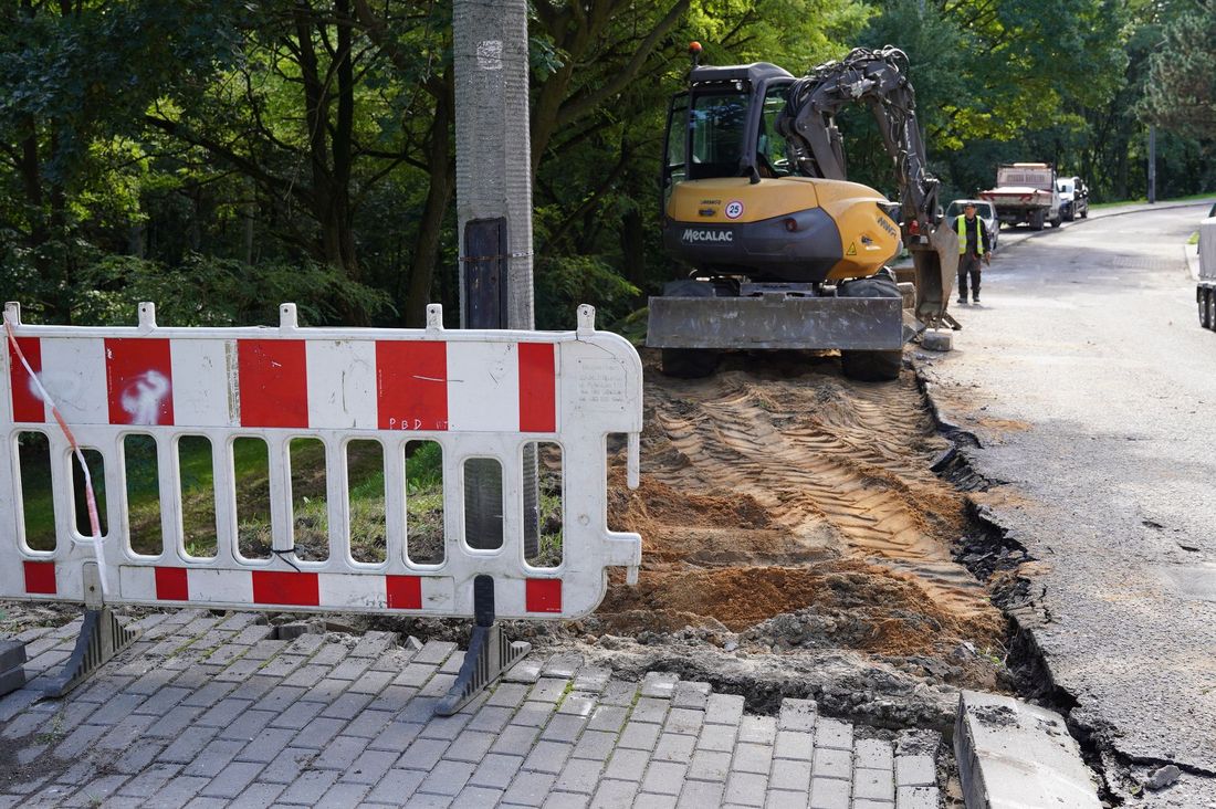Remontowane pobocze, w tle koparka przed rozkopanym chodnikiem