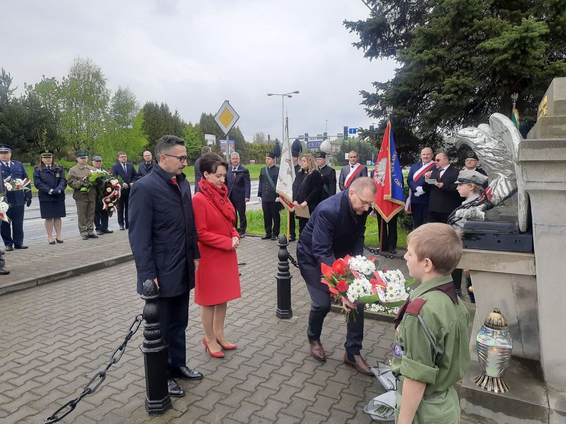 Zdjęcie przedstawia składanie kwiatów pod pomnikiem.