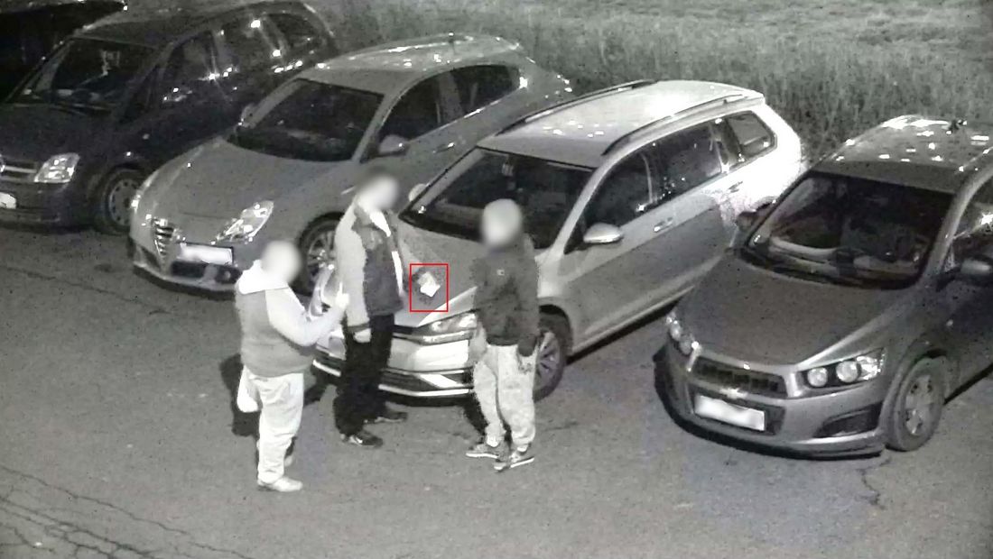 Trzej mężczyźni stoją na parkingu, za nimi cztery samochody