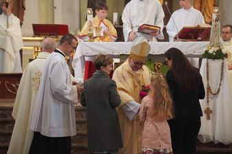 Arcybiskup przyjmuję kwiaty od wiernych przed ołtarzem. Wokół stoją inni duchowni.