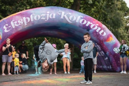 Chłopak wykonuje salto w tył podczas pokazu tanecznego przed zgromadzoną publicznością i dmuchaną bramą