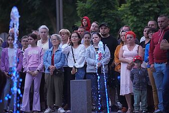 Zbliżenie na grupę widzów stojących za strumieniami błękitnej wody; na pierwszym planie kobieta w białej bluzce i kobieta w denimowej kurtce