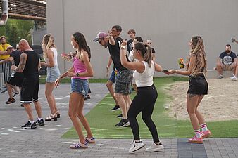 Grupa osób tańcząca w rzędzie na sztucznej trawie podczas festiwalu plenerowego