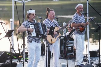 Czterej muzycy w pasiatych koszulkach grają koncert pod białym namiotem. Od lewej: skrzypek, akordeonista, gitarzysta i mandolinista