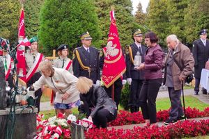 Zdjęcie przedstawia składanie kwiatów pod pomnikie. 