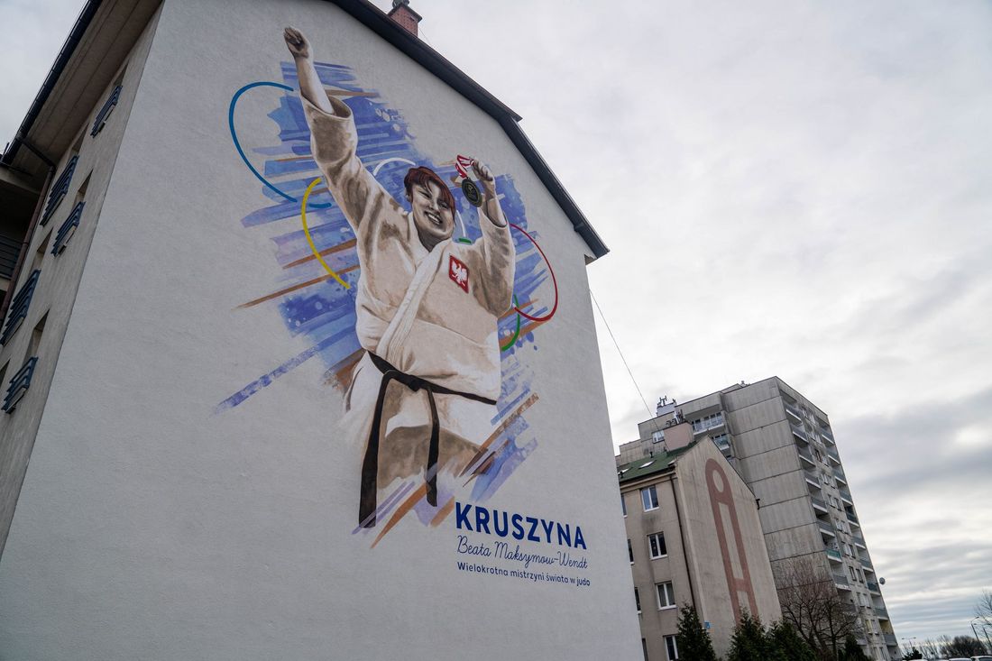 Mural z Beatą Maksymow-Wendt - ubranej w białe komono z godłem Rzczeczpospolitej Polski, trzymająca w uniesionej lewej dłoni medal. Za nią koło symbolizujące Igrzysta Olimpijskie. Na dole napis Kruszyna, Beata Maksymow-Wendt - wielokrotna mistrzyni świata w judo