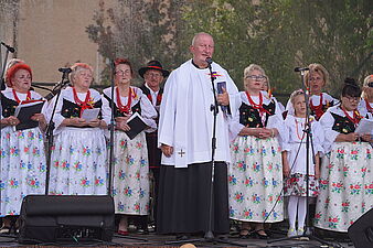 Ksiądz ze sceny odprawia nabożeństwo dożynkowe w tle zespół Jastrzymbioki