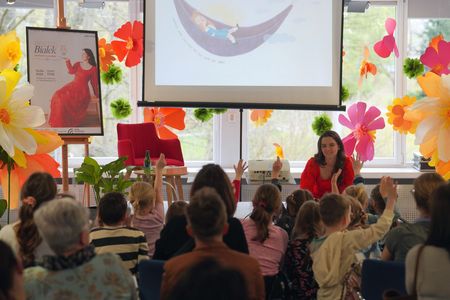 Ujęcie z tyły dzieci podnoszą ręce do góry przed nimi siedzi sonia białek w tle plakat i ekran