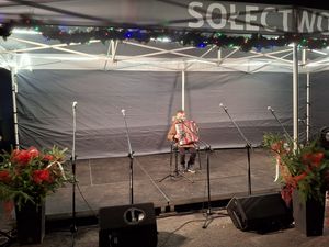 Dziecko gra na akordeonie na scenie pod namiotem z napisem „Sołectwo Bzie”, udekorowanym świątecznymi gałązkami i lampkami