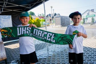 Dwaj młodzi piłkarze w klubowych koszulkach trzymający wspólnie zielony szalik z napisem „UKS ORZEŁ Moszczenica”