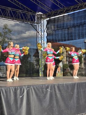 Zespół cheerleaderek w różowo-niebieskich strojach dający pokaz tańca z pomponami na zadaszonej scenie