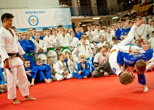 Walka judo - moment powalenia jednego z zawodników. Obok sędzia obserwuje walkę oraz widownia pozostałych judoków