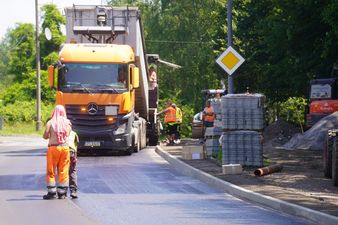 robotnicy stoją na drodze, w tle wywrotka w kolorze pomarańczowym