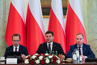Prezydium siedzi na tle flag Polski