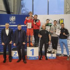 Zawodnicy stojący na stopniach podium, z nimi trenerzy.