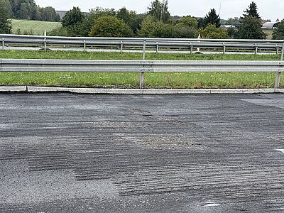 Sfrezowana i porysowana nawierzchnia asfaltowa jezdni przy barierze ochronnej