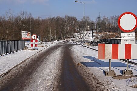 Wjazd na plac budowy drogi ze znakami zakazu ruchu, barierami i ośnieżonym poboczem