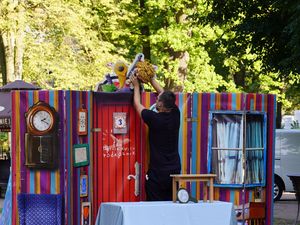 Mężczyzna ustawia kukiełkę na szczycie kolorowej, pasiastej parawany teatralnej podczas spektaklu plenerowego