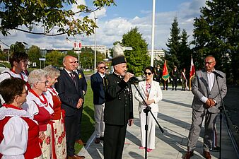 Przemówienie mężczyzny w galowym mundurze górniczym podczas plenerowej uroczystości, w towarzystwie osób w strojach ludowych i oficjalnych oraz pocztów sztandarowych.