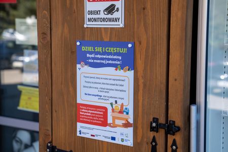 Lodówka społeczna przy ośrodku pomocy społecznej. Na niej kartka z napisem dziel sie i czestuj. Badź odpowiedzialny - nie marnuj jedzenia
