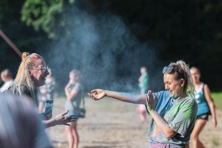 Kobieta obsypuje drugą dziewczynę kolorowym proszkiem, tworząc wokół niej barwną chmurę pyłu