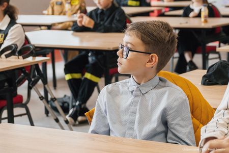 Chłopak w okularach patrzacy prawdopodobnie na przemawiających