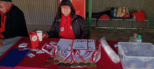 Pani siedząca przy stanowisku z pamiątkowymi medalami oraz dyplomami
