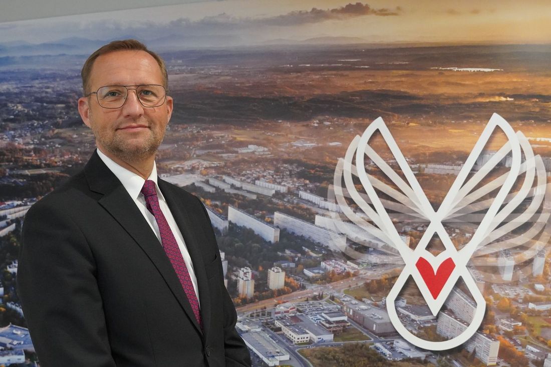 Sekretarz Miasta Jastrzębie-Zdrój w garniturze na tle ścianki miasta