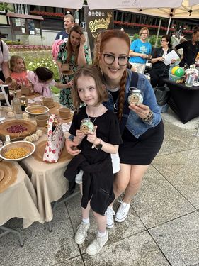Kobieta i dziewczynka z uśmiechem prezentują własnoręcznie zrobione, zielone sole do kąpieli w słoiczkach podczas warsztatów ekologicznych.