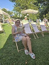 kobieta siedzi na leżaku i czyta ksiażkę
