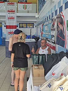 Dwie osoby stoją przy stoliku organizacyjnym i rejestrują się na zawody pływackie