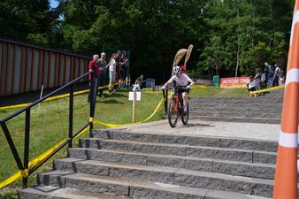 Zawodnik MTB w białym stroju jedzie rowerem po płaskim fragmencie trasy tuż przed schodami