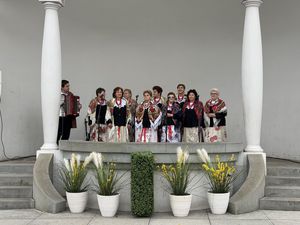 Kobiety z koła gospodyń wiejskich na scenie w kolorowych strojach śpiewają do mikrofonów obok stoi mężczyzna z akordeonem