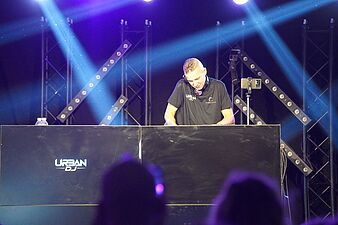 DJ miksujący muzykę za konsolą z logo „URBAN DJ” na tle reflektorów scenicznych