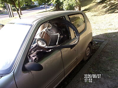 Srebrny Fiat Seicento z wybitym bocznym oknem, z którego wystaje opona rowerowa i mały wózek