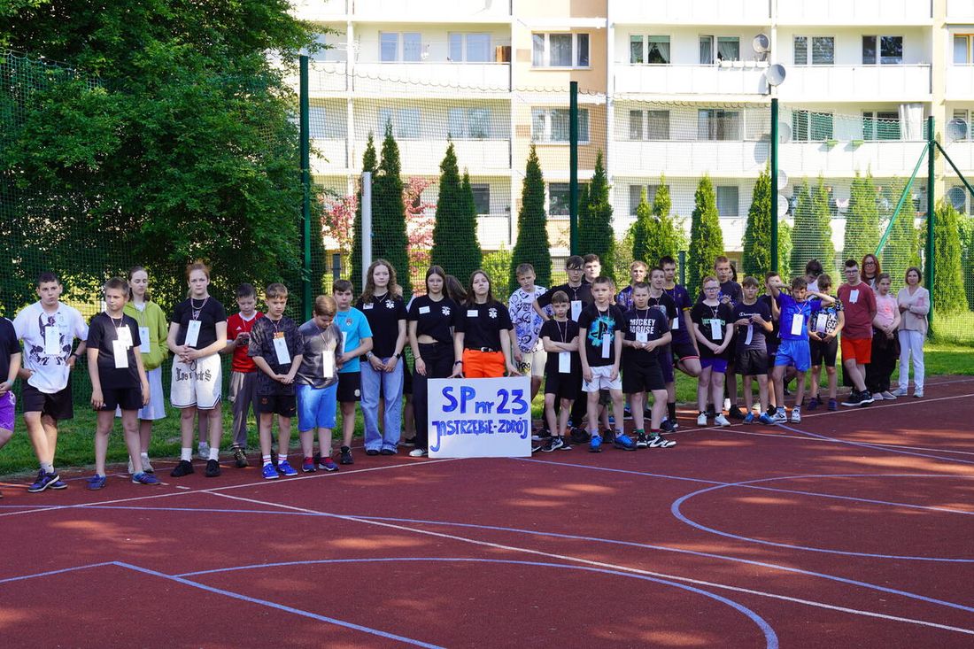uczestnicy spartakiady w strojach sportowych stoją na boisku w Szkole Podstawowej nr 23