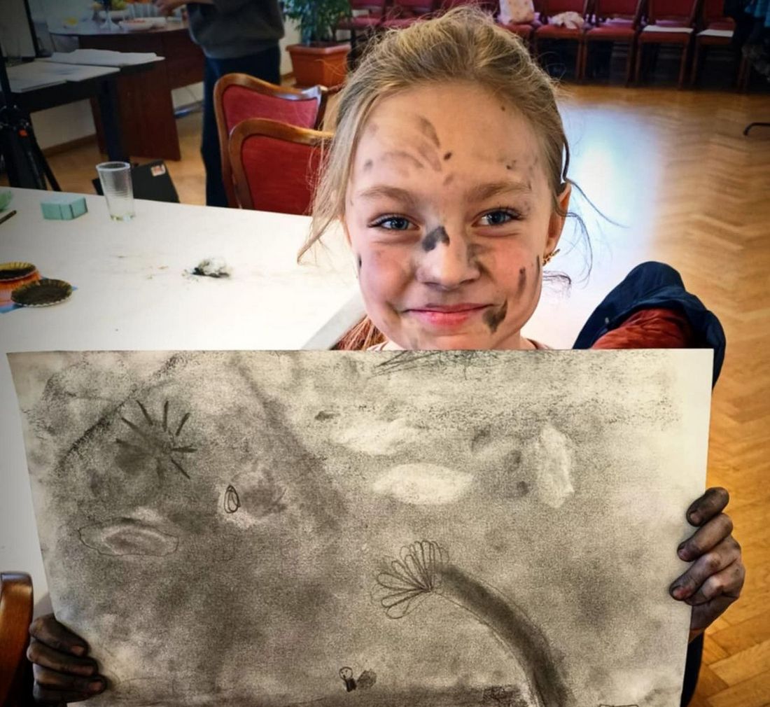 Dziewczynka trzymająca pracę zrobiona podczas warsztatów plastycznych.