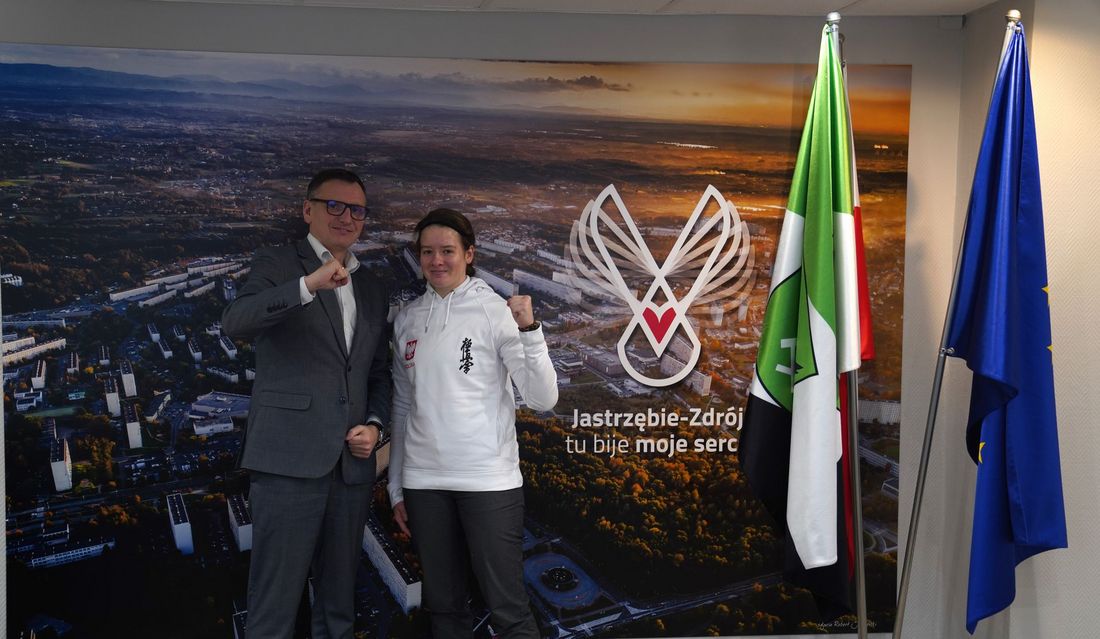 Michał Urgoł Prezydent Miasta Jastrzebie-Zdrój i Maria Franek pozują do zdjęcia z zacisniętymi pięściami, obok flaki Jastrzebia-Zdroju i Unii Europejskiej