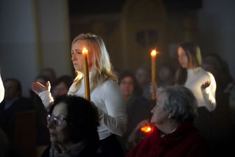 Dwie kobiety trzymają płonące świece, dookoła zebrani widzowie