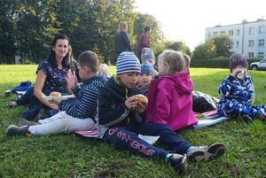 Uczestnicy pikniku kocykowego - grupa dzieci z opiekunem, siedząca na kocyku