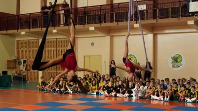 Dwie zawodniczki wykonują akrobacje powietrzne na szarfach zawieszonych pod sufitem hali sportowe