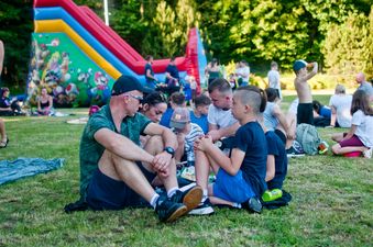 Grupa uczestników pikniku odpoczywa i rozmawia na trawie obok dmuchanej zjeżdżalni